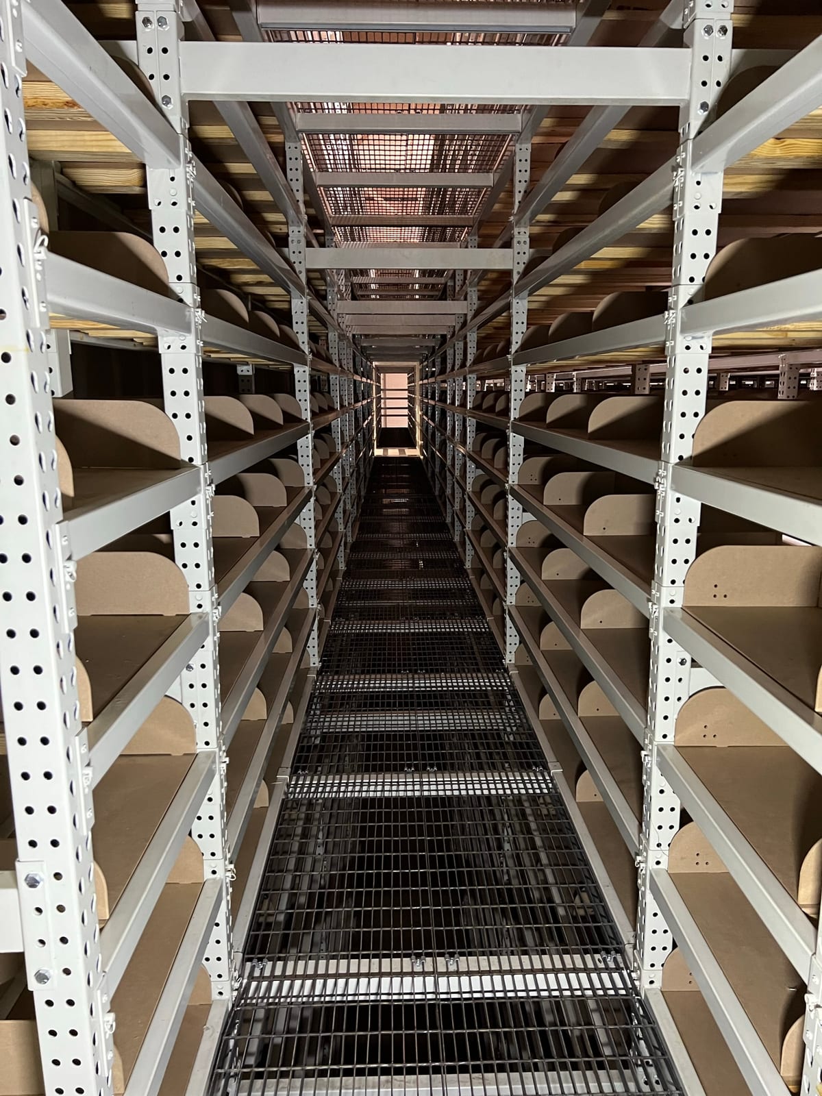 Narrow aisle between multi-level file folder storage shelving with wire walkway decking underfoot
